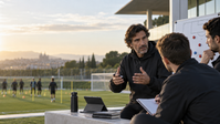 Coach discussing methodology with staff beside a football training pitch